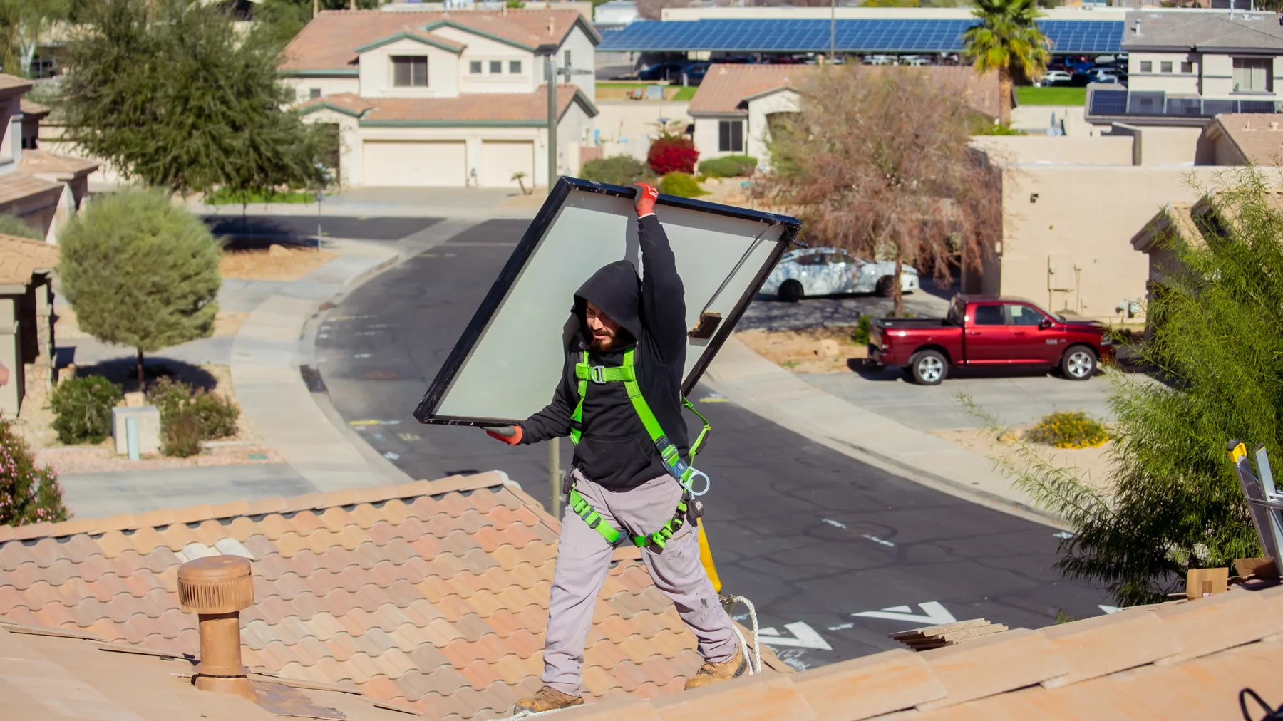 A Blackout Electric technician in a safety harness lifting a solar panel from a tile roof in the Phoenix metro