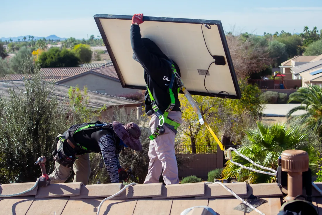 A technician carrying a solar panel across a tile roof during a detach and reset