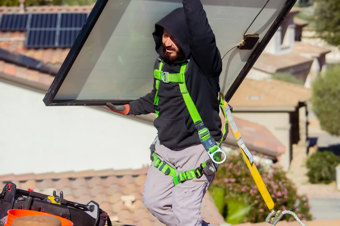 A Blackout Electric technician in a fall-arrest harness removing a solar panel